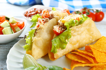 Tasty taco with nachos chips and vegetables on plate on table close up