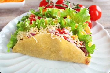 Tasty taco with vegetables on plate on table close up