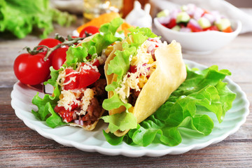 Tasty taco with vegetables on plate on table close up
