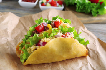 Tasty taco with vegetables on paper on table close up