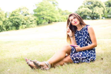 young woman thinking in the park holding a pen and notebook