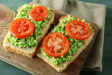 Vegan sandwich with avocado and vegetables on cutting board, on wooden background