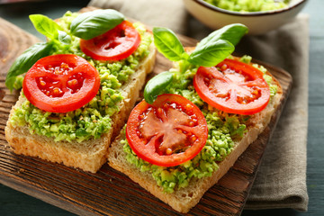 Vegan sandwich with avocado and vegetables on cutting board, on wooden background