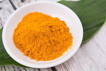 Turmeric powder and turmeric leaves over rustic wooden background