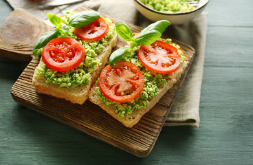 Vegan sandwich with avocado and vegetables on cutting board, on wooden background