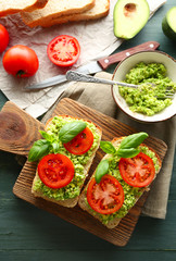 Vegan sandwich with avocado and vegetables on cutting board, on wooden background