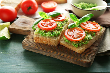 Vegan sandwich with avocado and vegetables on cutting board, on wooden background