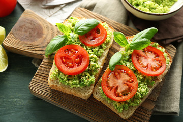 Vegan sandwich with avocado and vegetables on cutting board, on wooden background