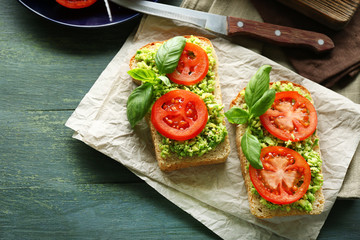 Vegan sandwich with avocado and vegetables on cutting board, on wooden background