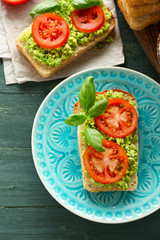 Vegan sandwich with avocado and vegetables on plate, on wooden background