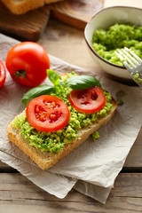 Vegan sandwich with avocado and vegetables on cutting board, on wooden background