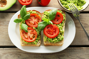 Vegan sandwich with avocado and vegetables on plate, on wooden background