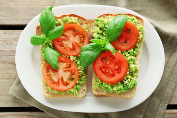 Vegan sandwich with avocado and vegetables on plate, on wooden background