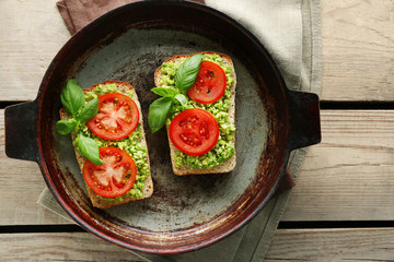 Vegan sandwich with avocado and vegetables on pan, on wooden background