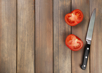 Halves of tomato with knife on wooden background