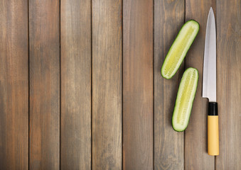Halves of cucumber with knife on wooden background