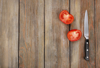 Halves of tomato with knife on wooden background