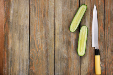 Halves of cucumber with knife on wooden background