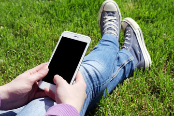 Young woman with mobile phone sitting on green grass outdoors