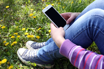 Young woman with mobile phone sitting on green grass outdoors