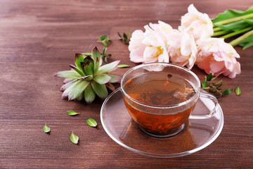 Cup of herbal tea with tulips on wooden table, closeup