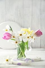 Spring bouquet in glass mug on color wooden background