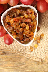 Raisins in bowl with grapes on table close up