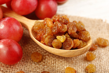Raisins in wooden spoon with grapes on table close up