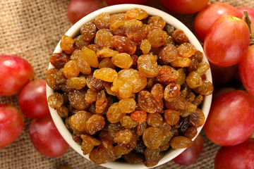 Raisins in bowl with grapes on table close up