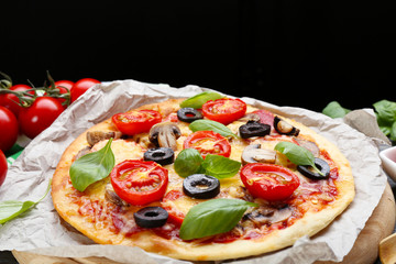 Tasty pizza with vegetables and basil on black background