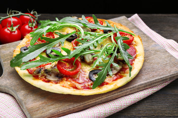Tasty pizza with vegetables and arugula on cutting board on table close up