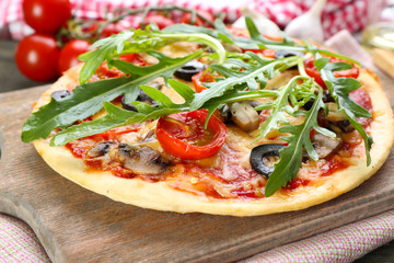 Tasty pizza with vegetables and arugula on cutting board on table close up