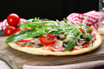 Tasty pizza with vegetables and arugula on cutting board on table close up