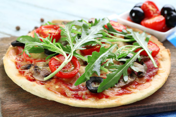 Tasty pizza with vegetables and arugula on cutting board on table close up
