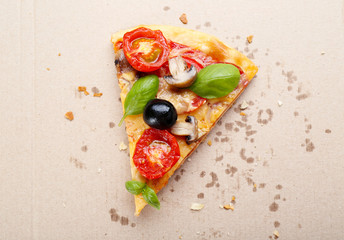 Slice of tasty pizza with vegetables and basil in cardboard box close up