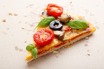 Slice of tasty pizza with vegetables and basil in cardboard box close up