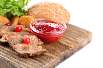 Beef with cranberry sauce, roasted potato slices and bun on wooden board, isolated on white