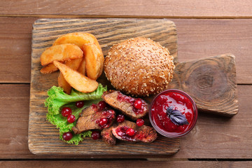 Beef with cranberry sauce, roasted potato slices and bun on cutting board, on wooden background