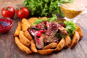 Beef with cranberry sauce, roasted potato slices and bun on wooden cutting board, close-up