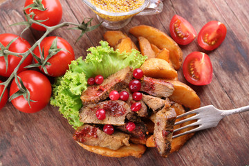 Beef with cranberry sauce, roasted potato slices and bun on cutting board, on wooden background