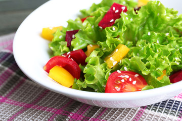 Bowl of fresh green salad on table with napkin, closeup