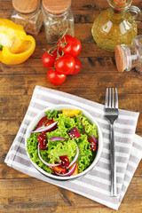 Bowl of fresh green salad on table with napkin, closeup