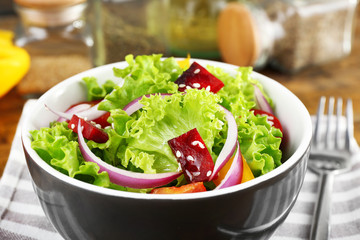 Bowl of fresh green salad on table with napkin, closeup