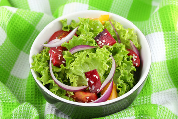 Bowl of fresh green salad on table with napkin, closeup