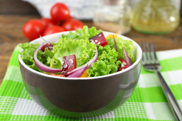 Bowl of fresh green salad on table with napkin, closeup