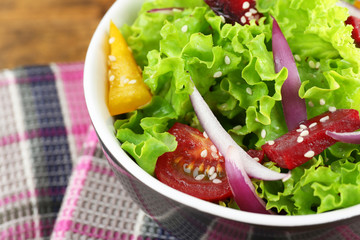 Bowl of fresh green salad on table with napkin, closeup