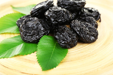 Pile of prunes with leaves on wooden tray, closeup