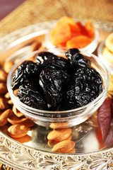 Pile of prunes in glass saucers with grape leaves, closeup