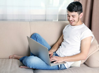 Handsome young man sitting on sofa and using laptop in room