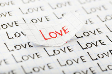 Word LOVE written on torn paper on sheet of paper background